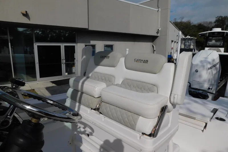 Slide: The Image of 2023 Caymas 28 HB boat with cushioned seating and steering wheel, docked near a building. - 12