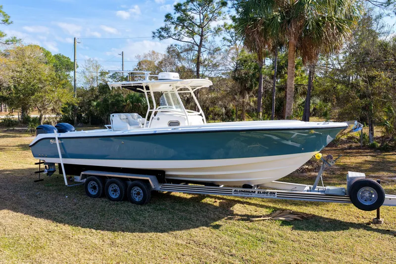 Slide: The Image of 2011 Edgewater 318CC boat on trailer, parked on grass with trees in background. - 31