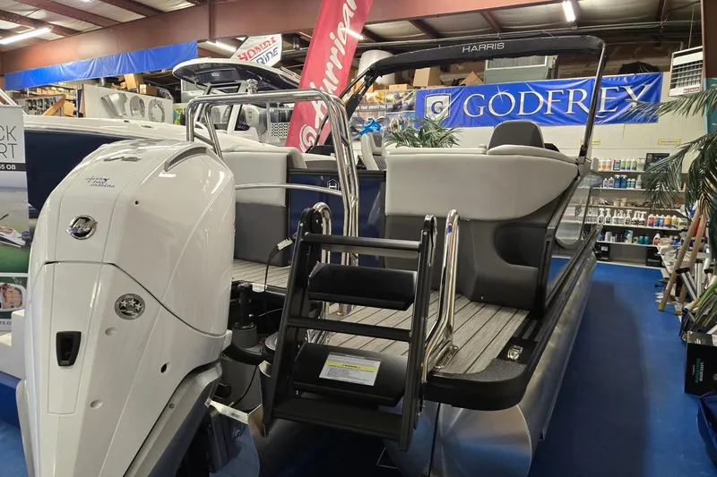 Slide: The Image of 2026 Harris Sunliner 230 pontoon boat displayed indoors with outboard motor. - 5