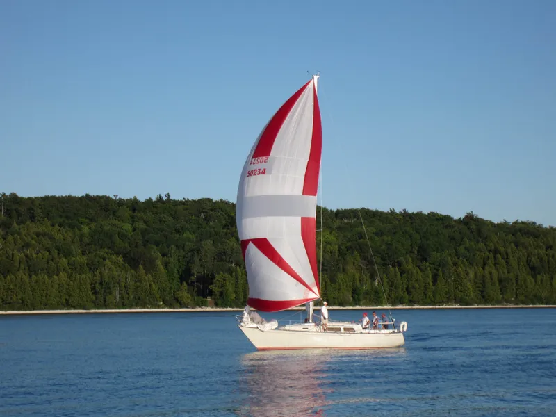 The Image of 1985 C&C 37 sailboat with red and white sail on calm water. - 0