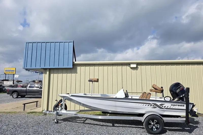 Slide: The Image of 2026 Xpress H18 boat on trailer, parked beside a beige building under cloudy sky. - 5