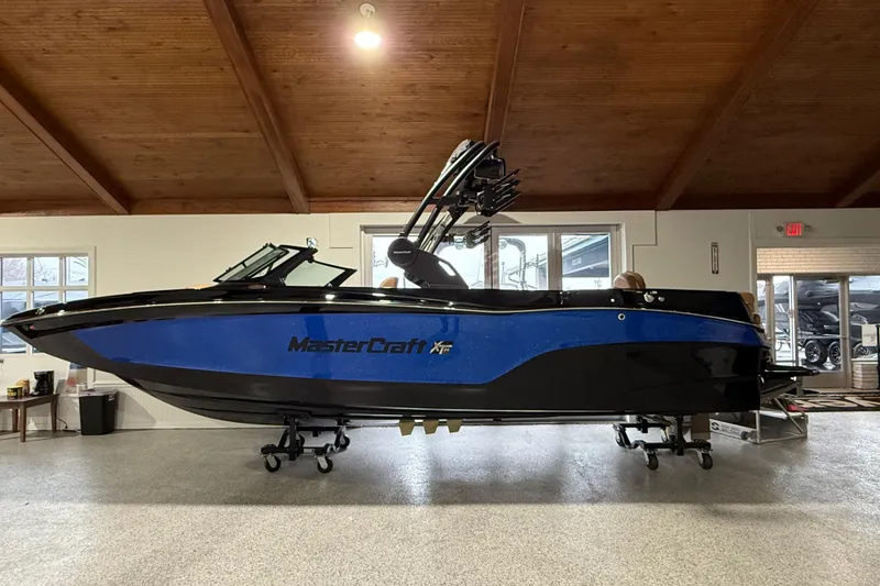 The Image of 2026 MasterCraft XT24 boat in showroom, blue and black design, side view. - 0