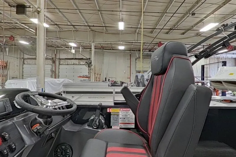 Slide: The Image of 2026 Bennington 23 SSBSF boat interior with steering wheel and red-trimmed seat in a warehouse. - 23