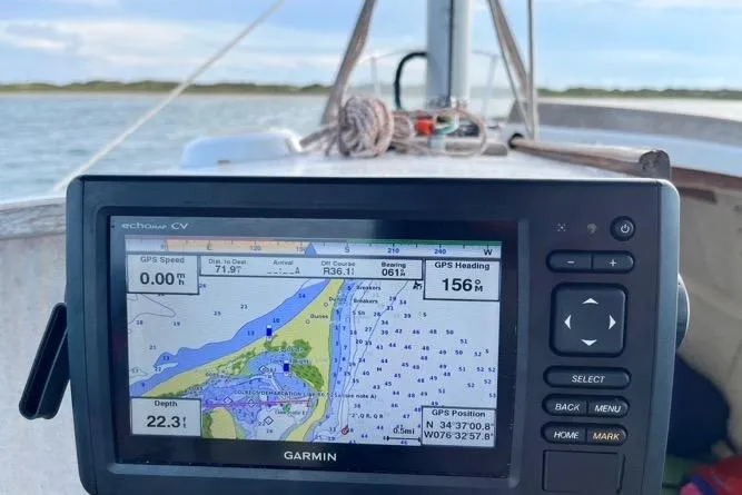 Slide: The Image of 1976 Custom Wooden Sloop on trailer, surrounded by trees and other boats. - 7