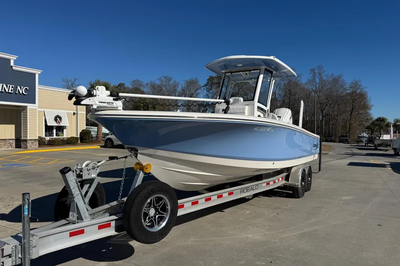 Slide: The Image of 2023 Robalo 266 Cayman boat on trailer, parked outside a building under clear blue sky. - 6