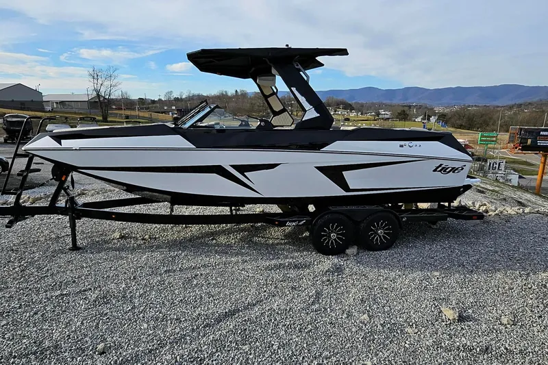 Slide: The Image of 2026 Tigé 24RZX boat on trailer, sleek design, parked on gravel with scenic background. - 24