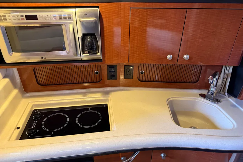 Slide: The Image of 2005 Sea Ray Sundancer 320 galley with microwave, stove, sink, and wooden cabinetry. - 28