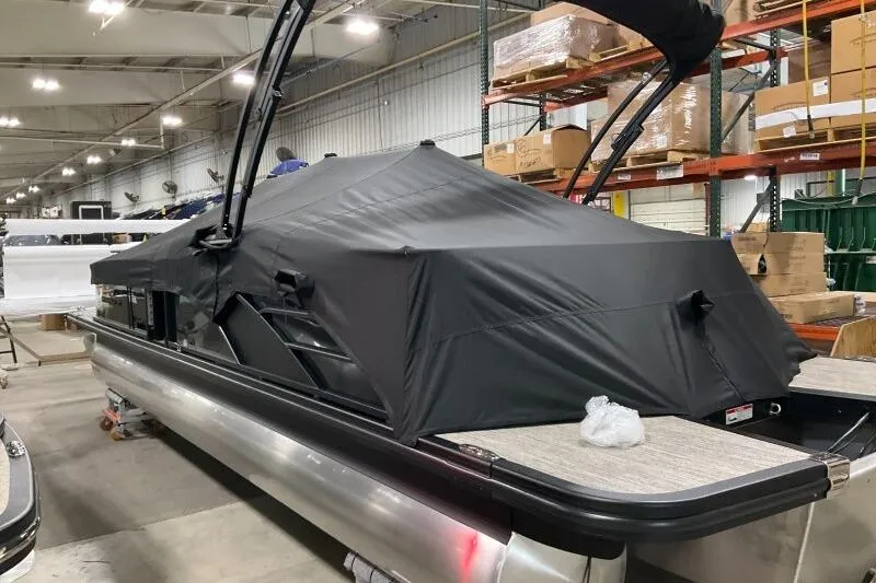 Slide: The Image of 2026 Bennington 25 LTSBSF pontoon boat with black cover in a warehouse setting. - 24