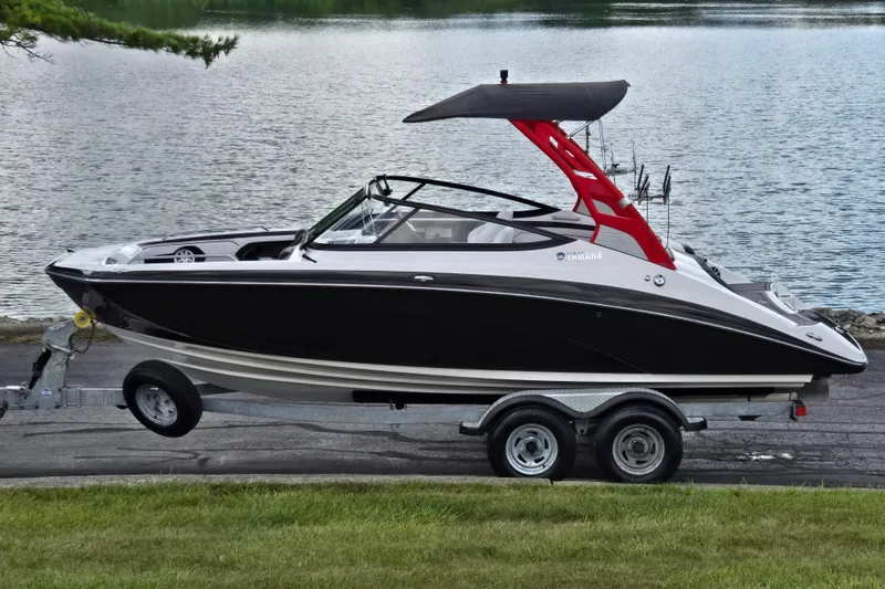 Slide: The Image of 2018 Yamaha Boats 212X on trailer by a lake, featuring sleek black design. - 0