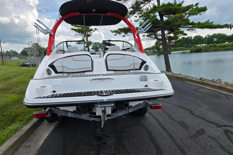 Slide: The Image of 2018 Yamaha Boats 212X on trailer by a lakeside, showcasing rear deck and seating. - 2