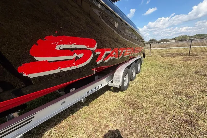 Slide: The Image of 2018 Statement 380 Open boat on trailer, featuring bold red logo, parked on grass. - 7