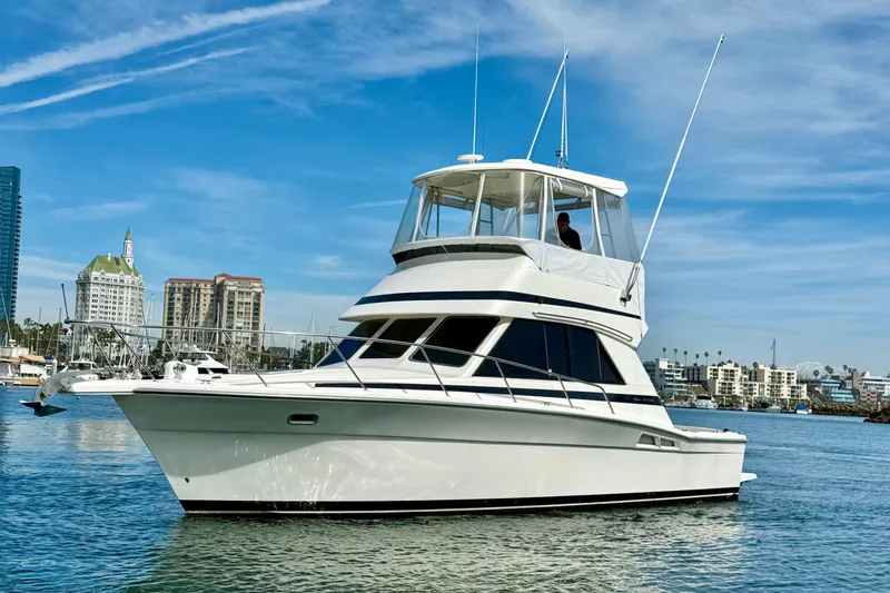 Slide: The Image of 1998 Riviera 34 Convertible yacht cruising in a scenic harbor with city skyline backdrop. - 3