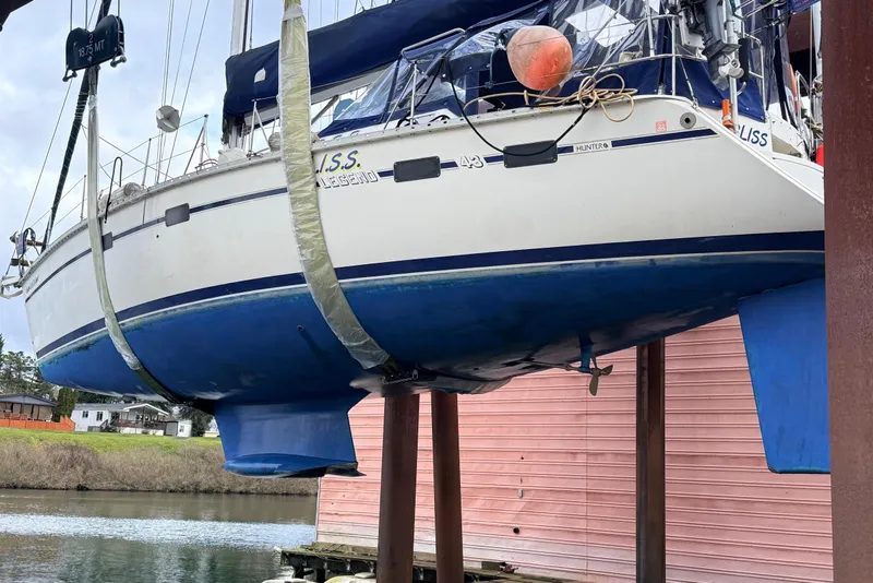 Slide: The Image of 1992 Hunter Legend 43 sailboat suspended for maintenance near a waterfront building. - 50