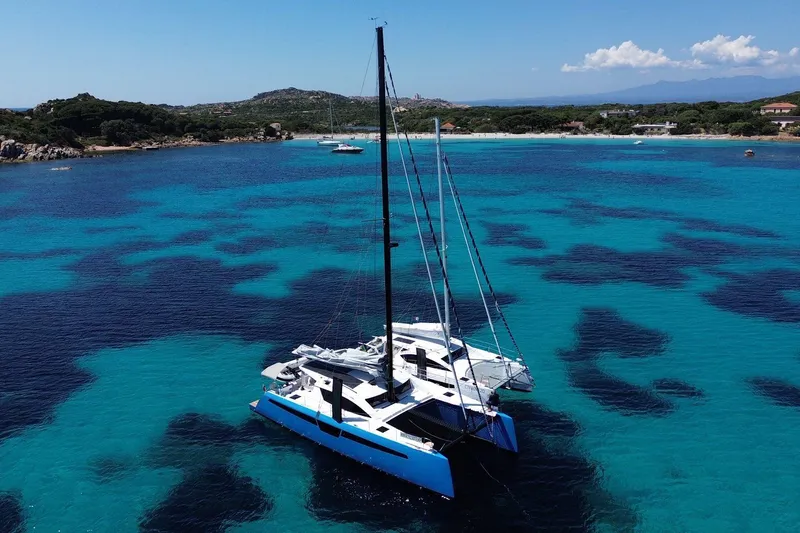 Slide: The Image of 2025 C-Catamarans 48 sailing in clear turquoise waters near a scenic coastline. - 2