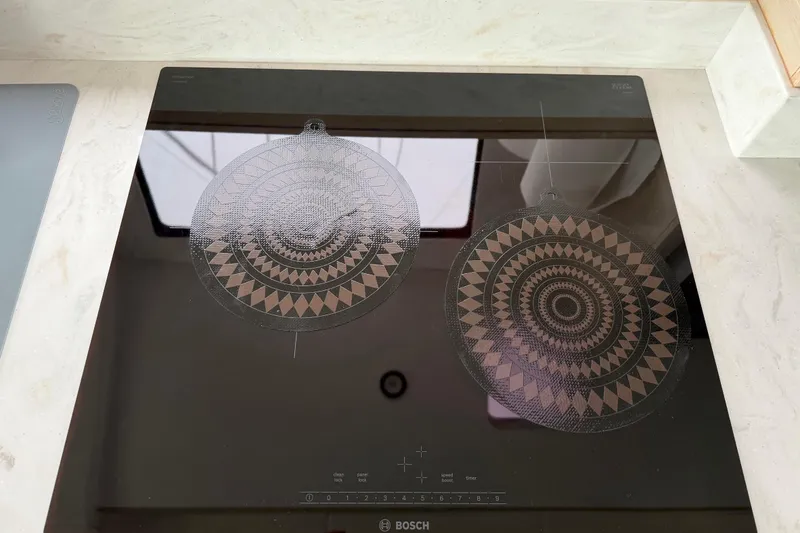 Slide: The Image of Modern Bosch induction cooktop with geometric patterned trivets on a C-Catamarans 48, 2025 model. - 64