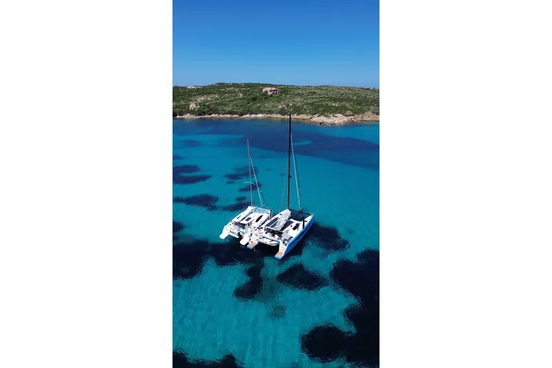 Slide: The Image of 2025 C-Catamarans 48 sailing in clear turquoise waters near a rocky coastline. - 7