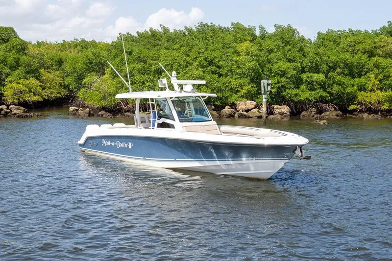 Slide: The Image of 2019 Boston Whaler 380 Outrage boat cruising near lush green shoreline. - 1