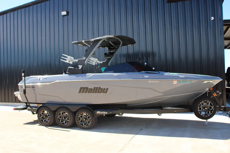 Slide: The Image of 2020 Malibu Wakesetter 25 LSV boat on trailer, parked by black building. - 2