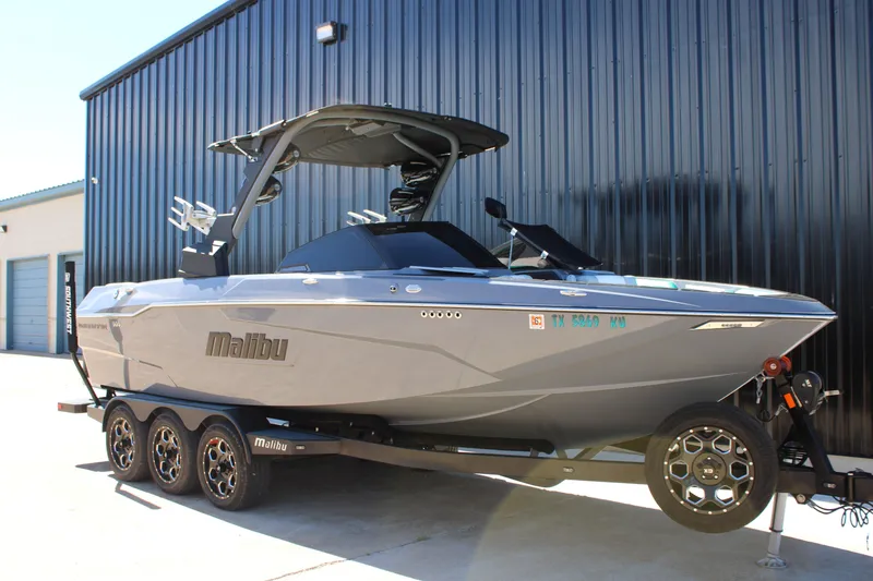 Slide: The Image of 2020 Malibu Wakesetter 25 LSV boat on trailer, parked by a black building. - 3