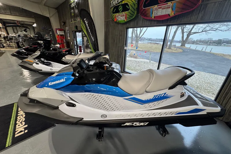 Slide: The Image of 2026 Kawasaki STX160X jet ski in showroom, blue and white design, side view. - 3
