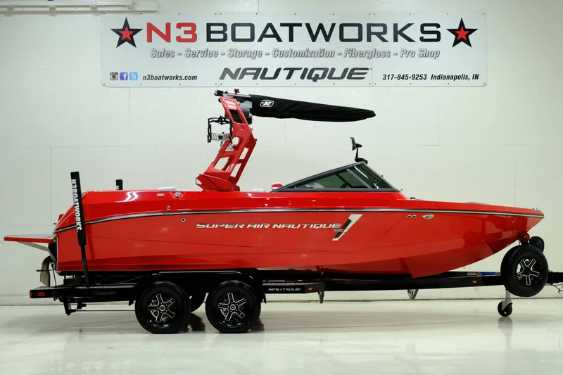 The Image of Red 2018 Nautique 210 boat on trailer in showroom. - 1
