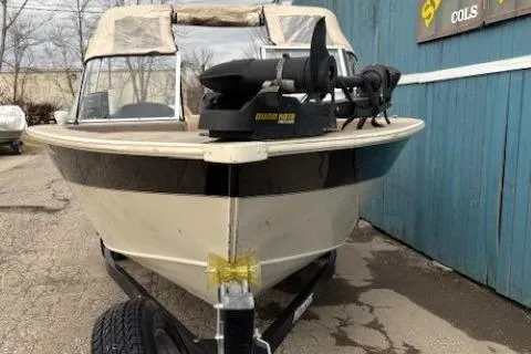 Slide: The Image of 2003 Monark King 190 boat with trolling motor, parked on a trailer near a blue building. - 2