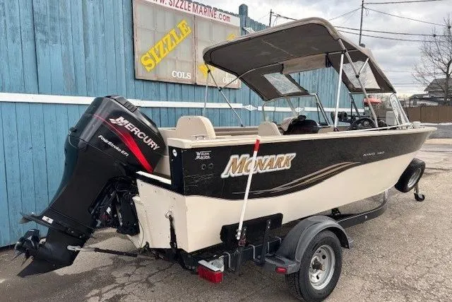 Slide: The Image of 2003 Monark King 190 boat with Mercury outboard motor on trailer, parked by blue building. - 6