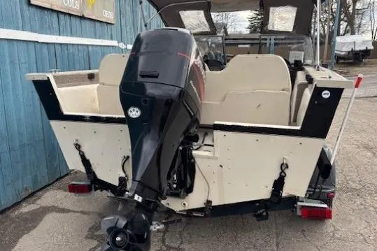 Slide: The Image of 2003 Monark King 190 boat with outboard motor, parked near a blue building. - 7