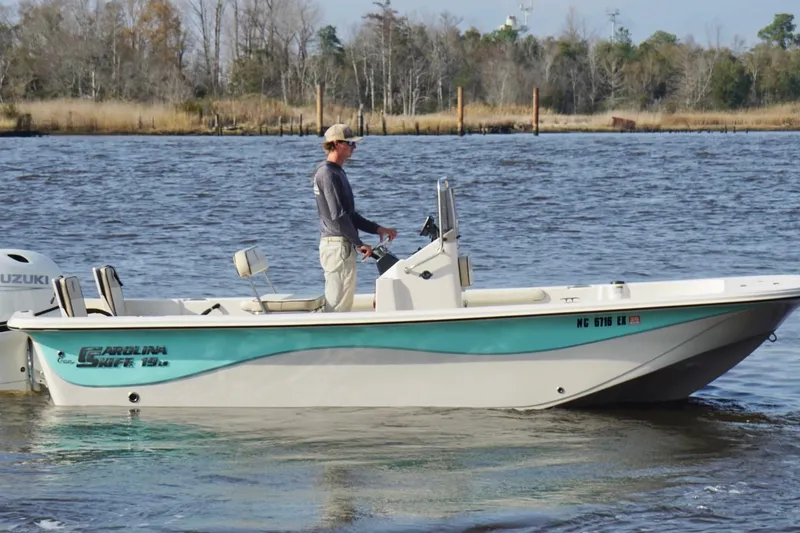 Slide: The Image of 2022 Carolina Skiff 19 LS boat on water, person steering, Suzuki engine visible. - 7