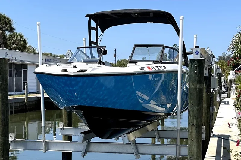Slide: The Image of 2023 Yamaha Boats AR250 on lift, blue hull, docked by canal. - 2
