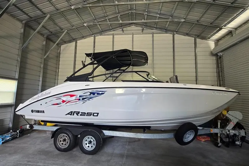 Slide: The Image of 2025 Yamaha Boats AR250 on trailer, parked outside blue building. - 0