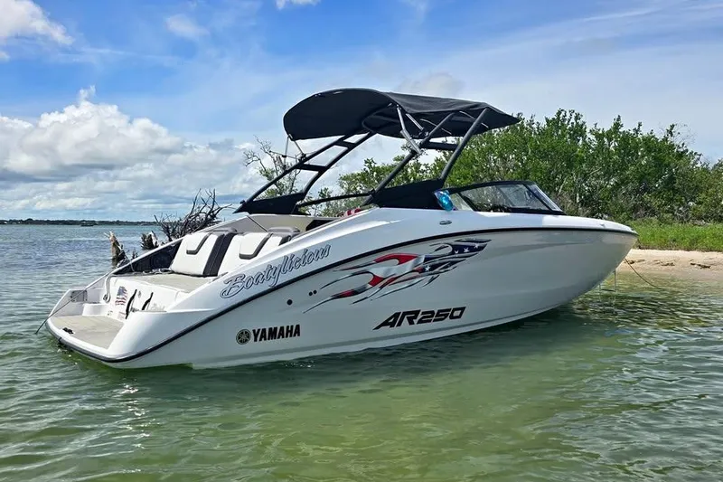 Slide: The Image of 2025 Yamaha Boats AR250 on trailer, parked outdoors near a house and palm trees. - 2