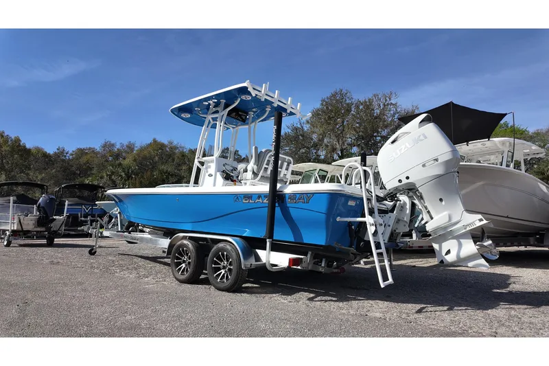 Slide: The Image of 2026 Blazer PureBay 2400 boat with Suzuki engine on trailer, parked outdoors. - 2