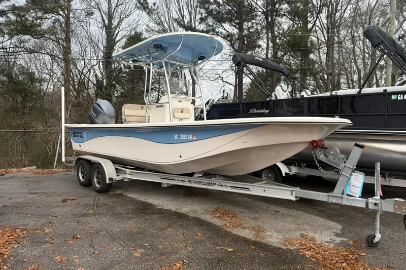 Slide: The Image of 2022 Carolina Skiff 23 LS boat on trailer, parked outdoors near trees. - 2