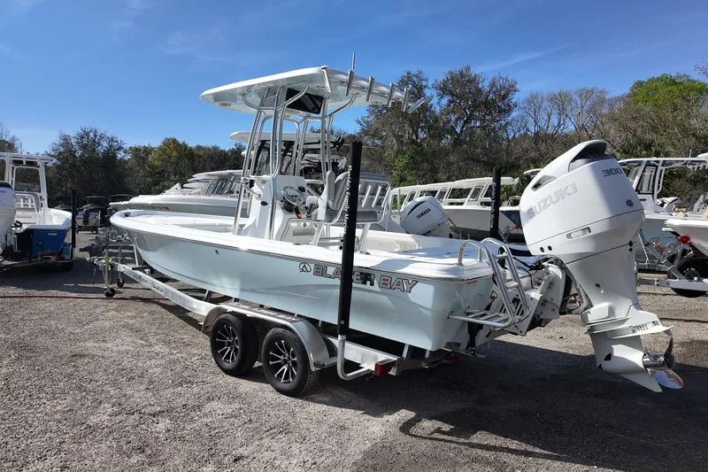 Slide: The Image of 2026 Blazer PureBay 2400 boat with Suzuki engine on trailer, parked outdoors. - 2