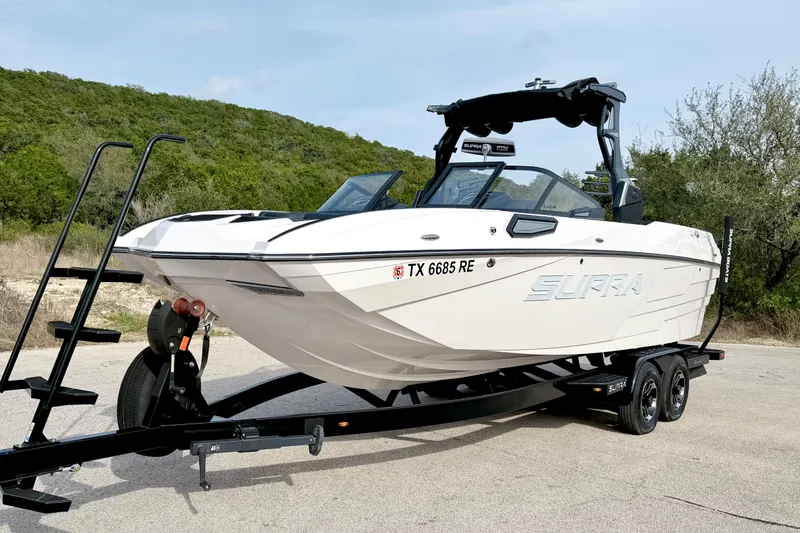 Slide: The Image of 2023 Supra SE 550 boat on trailer, parked outdoors with lush greenery background. - 11