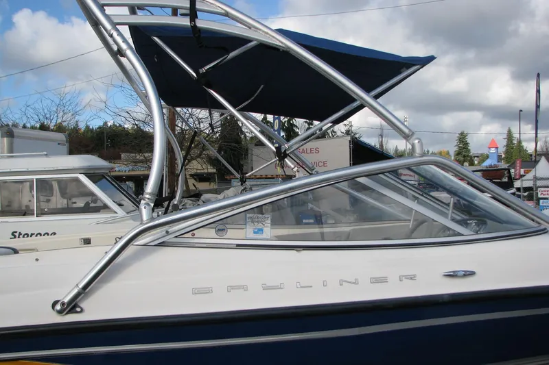 Slide: The Image of 2004 Bayliner 205 boat with blue canopy and sleek design, parked outdoors. - 2