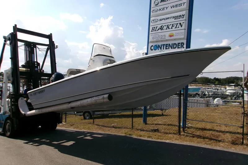 Slide: The Image of 2026 Key West 210 Bay Reef boat lifted by forklift near dealership sign. - 2