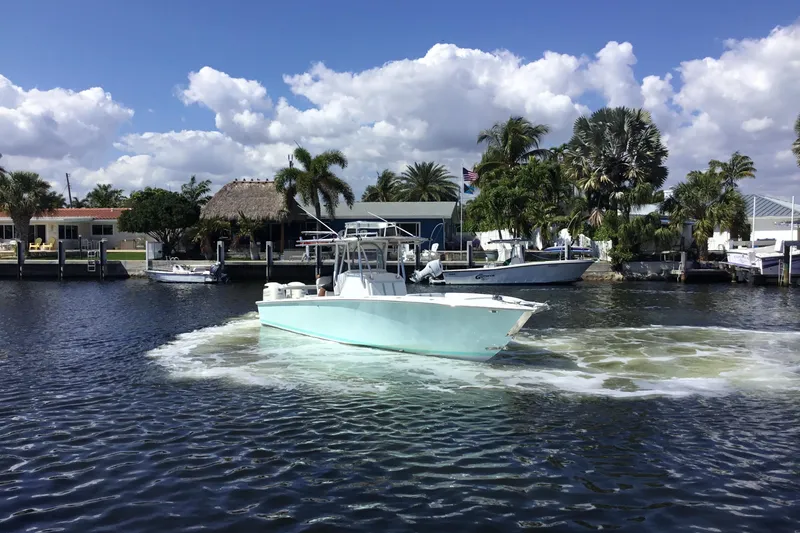 Slide: The Image of 2000 Jupiter 31 Center Console boat navigating a scenic waterfront with palm trees and docks. - 68
