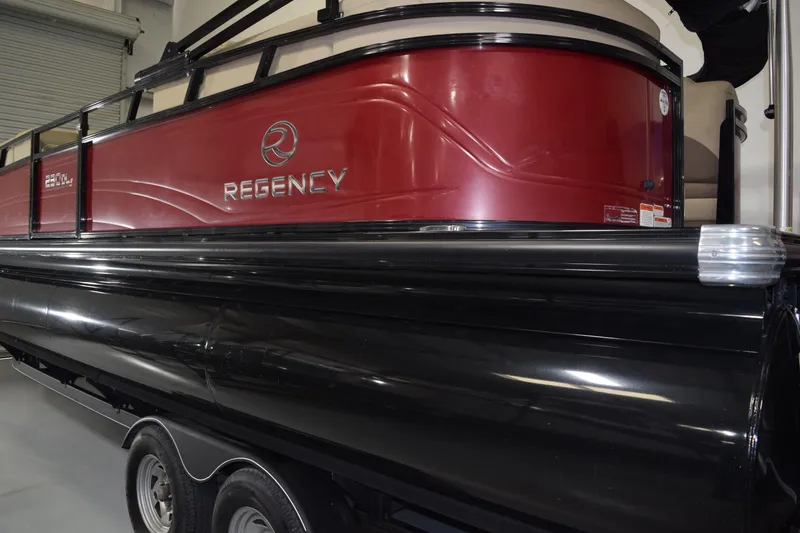 Slide: The Image of 2022 Regency 230 DL3 pontoon boat with red and black exterior in a showroom. - 2