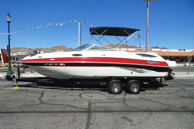 Slide: The Image of 2005 Kayot S245 boat on trailer, parked in urban setting under clear blue sky. - 1