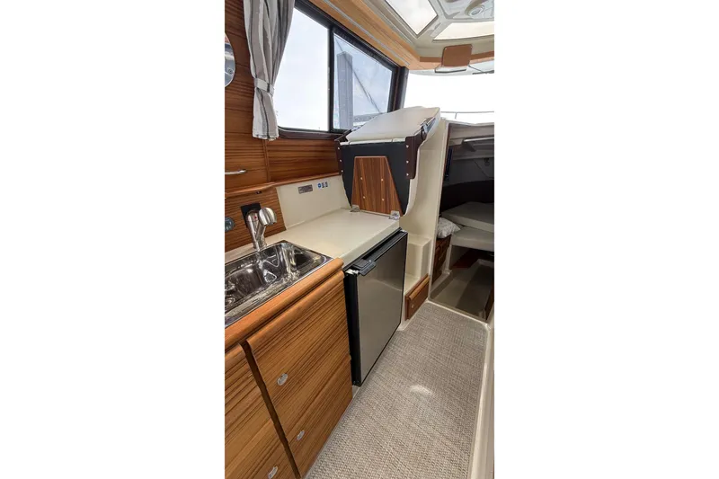 Slide: The Image of 2026 Ranger Tugs R-27 interior with kitchenette, featuring wood cabinetry and stainless steel sink. - 25