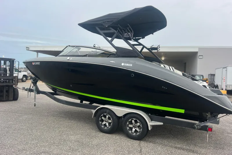 Slide: The Image of 2021 Yamaha Boats 255XD on trailer, sleek black design with green accent, parked outdoors. - 6