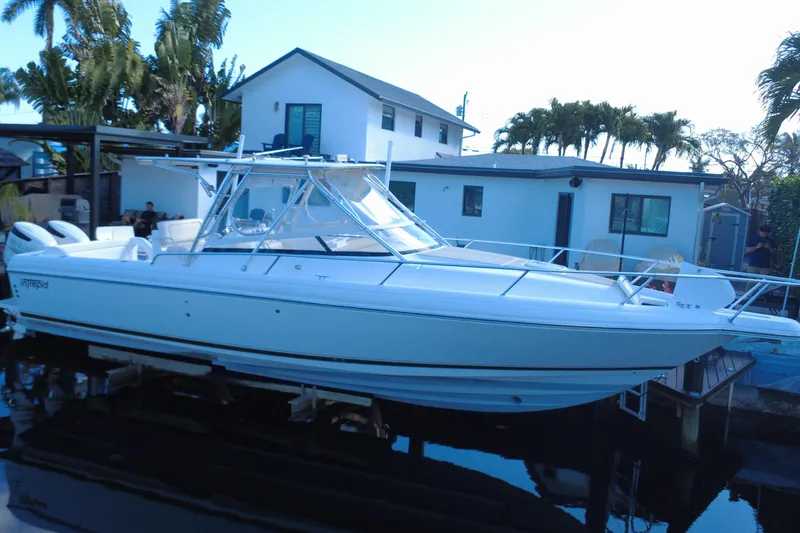 Slide: The Image of 2005 Intrepid 348 Walkaround boat docked near a house with palm trees. - 3