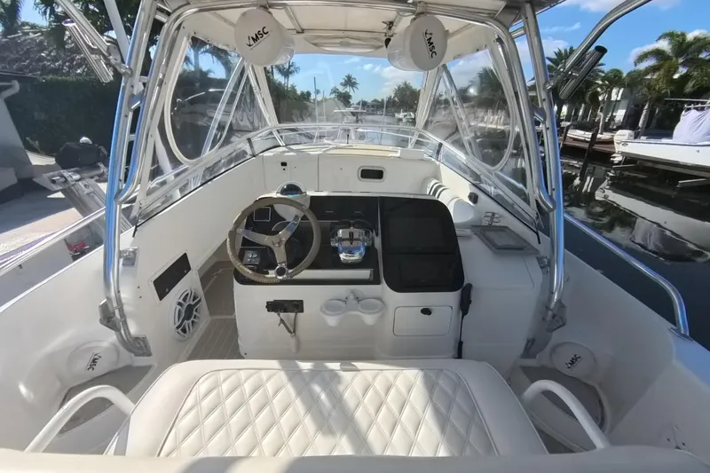 Slide: The Image of 2005 Intrepid 348 Walkaround boat interior with steering wheel and seating, docked by palm trees. - 33