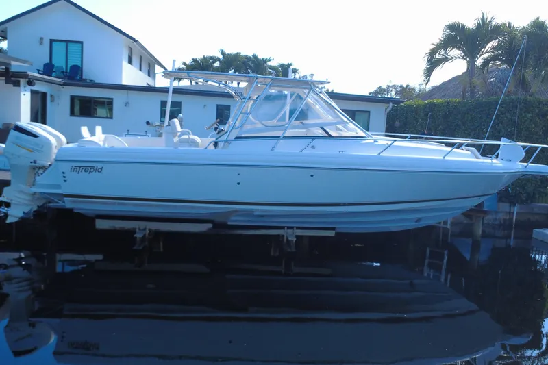 Slide: The Image of 2005 Intrepid 348 Walkaround boat docked near a modern house with palm trees. - 5