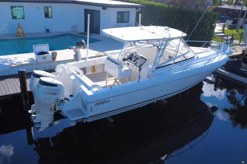 Slide: The Image of 2005 Intrepid 348 Walkaround boat docked near a poolside, featuring dual Suzuki engines. - 6