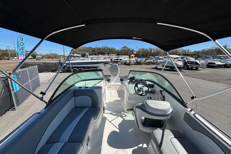 Slide: The Image of 2021 NauticStar 203 DC boat interior with seating and steering wheel, under canopy at dealership. - 16