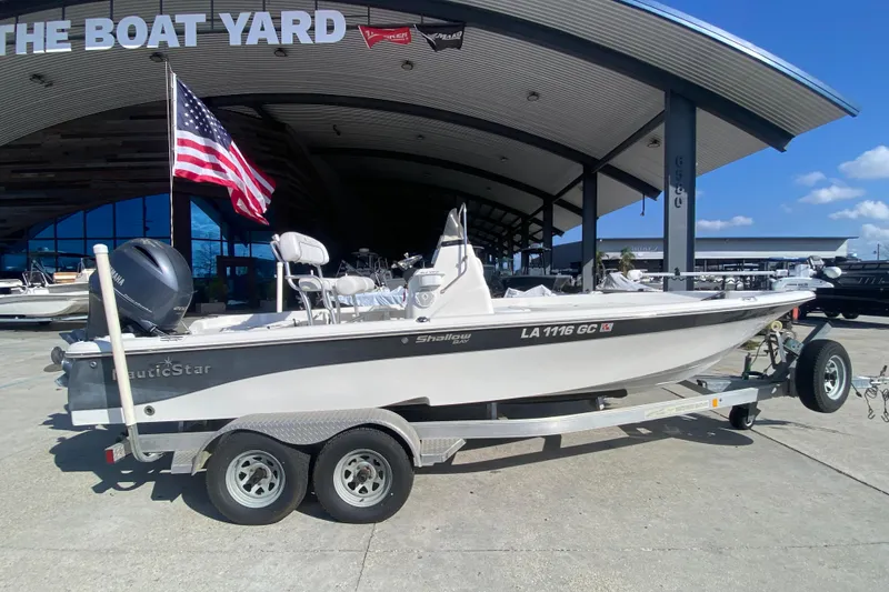 Slide: The Image of 2014 NauticStar 214 XTS Shallow Bay boat on trailer at dealership, American flag displayed. - 3
