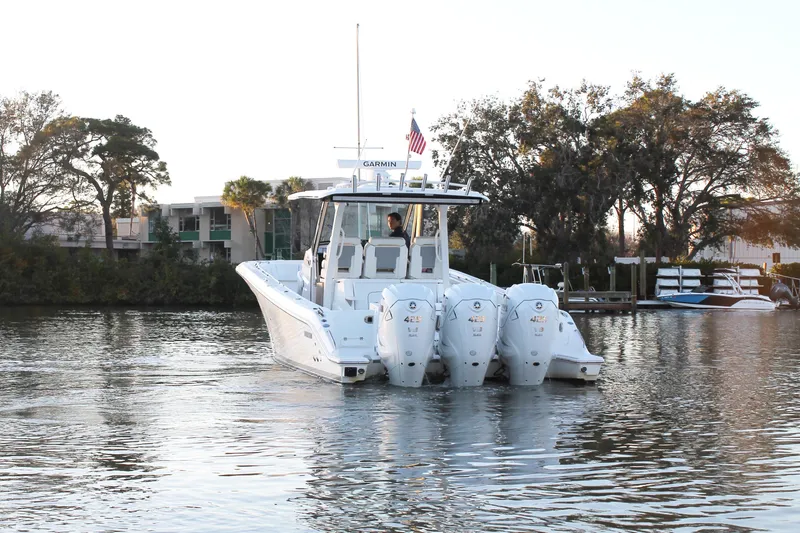 Slide: The Image of 2023 Pursuit S 378 Sport boat on calm water, surrounded by trees and docks. - 6